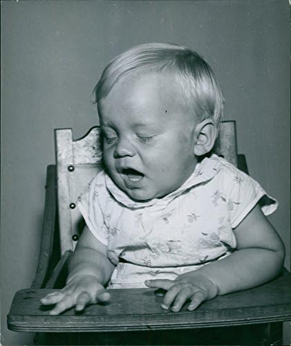 Гроздобер фотографија на бебе кое се мавта и седи на високо столче.